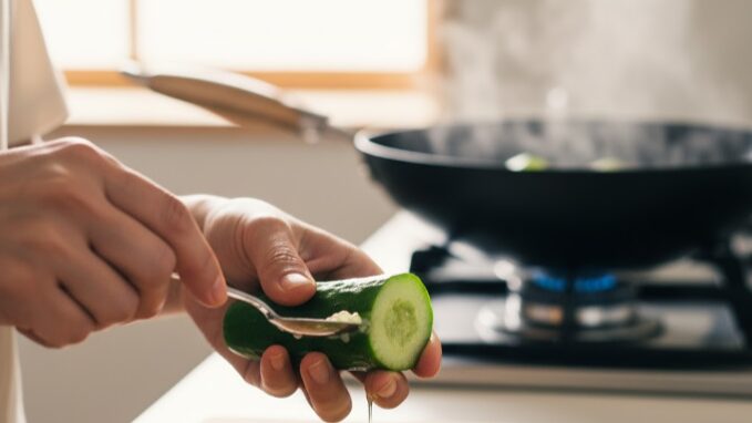 日本人女性の手が、半分に切ったきゅうりの中心部からスプーンでわたを丁寧に取り除いている様子。